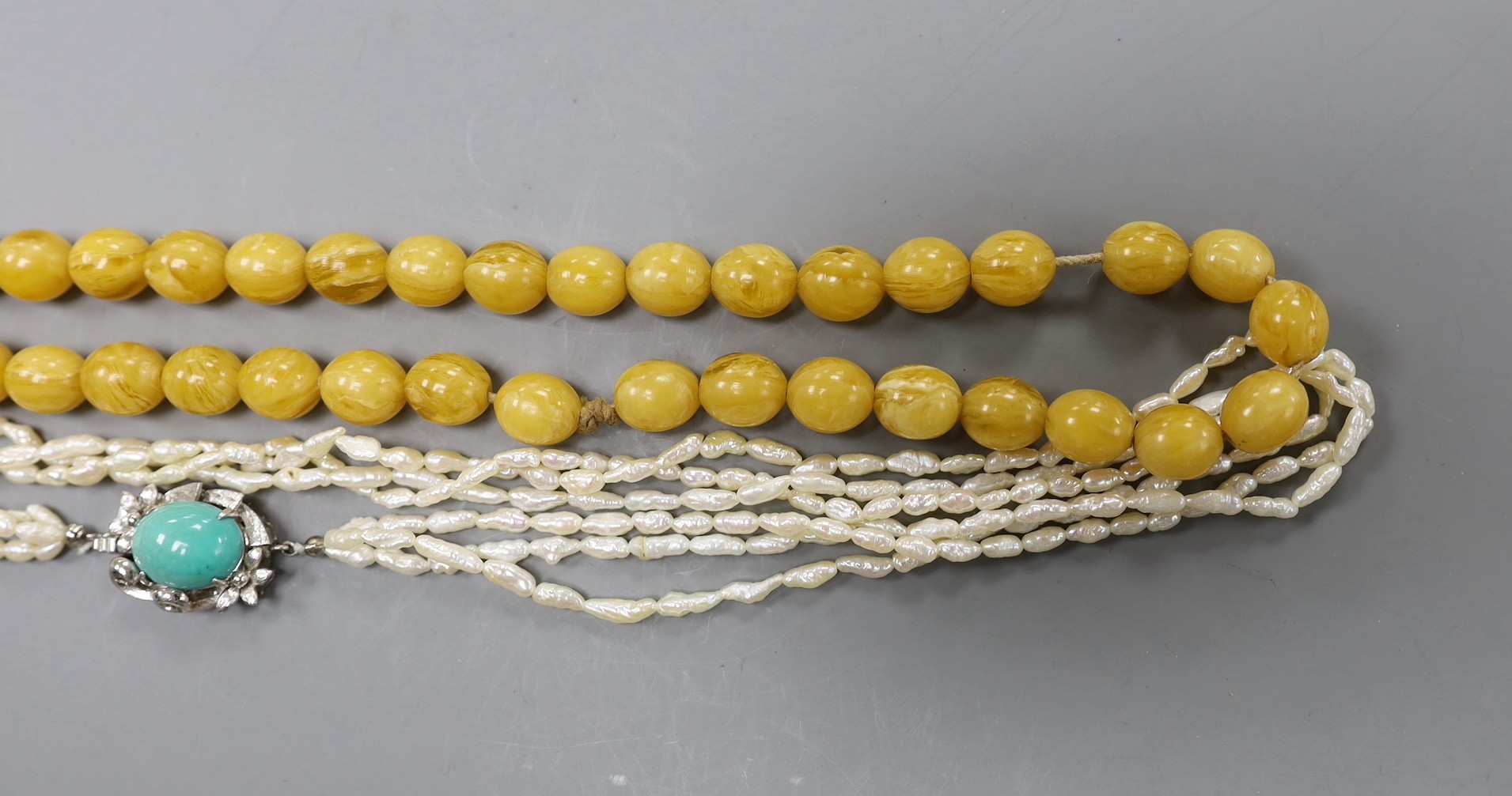A multi-strand 'rice pearl' necklace with 18k white metal and turquoise set clasp, 66cm and an amber necklace.